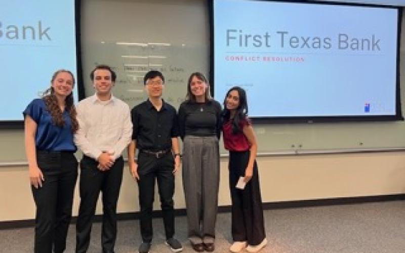 Five students stand and smile in front of a presentation slide titled "First Texas Bank"