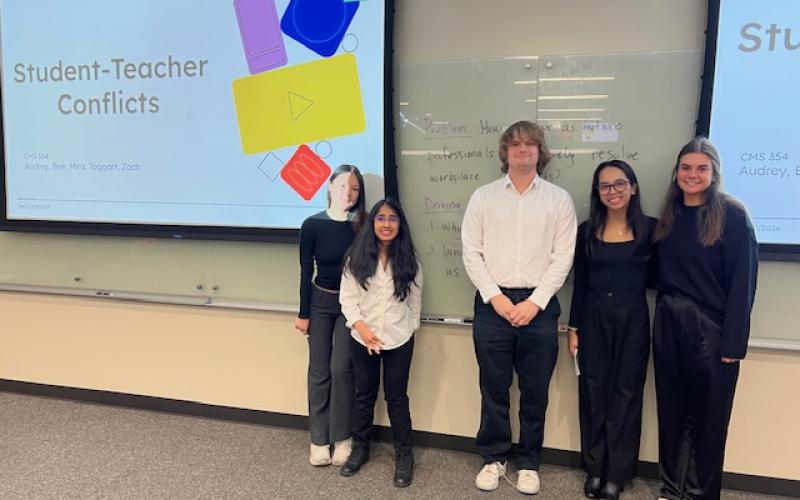 Five students standing in front of their presentation and smiling