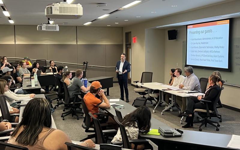 Image depicts a panel speaker presenting to a class.