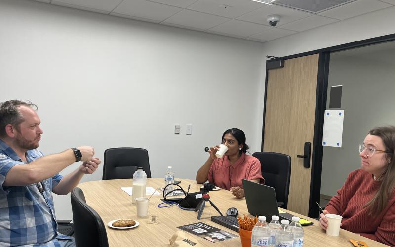 The image depicts one faculty member explaining an idea to two other faculty members.