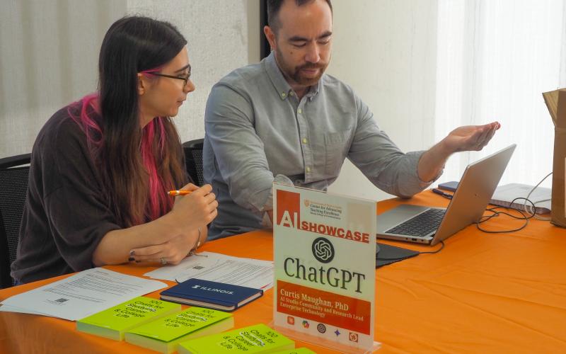 Two people seated at a table are discussing the content on a laptop computer. 