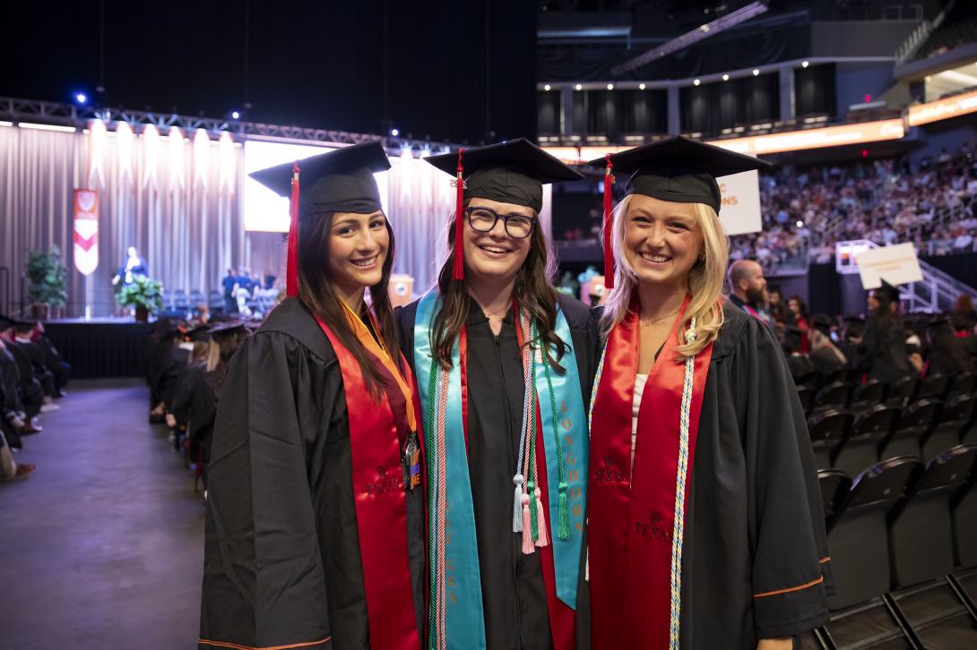 three moody graduates standing inside the moody center on graduation day